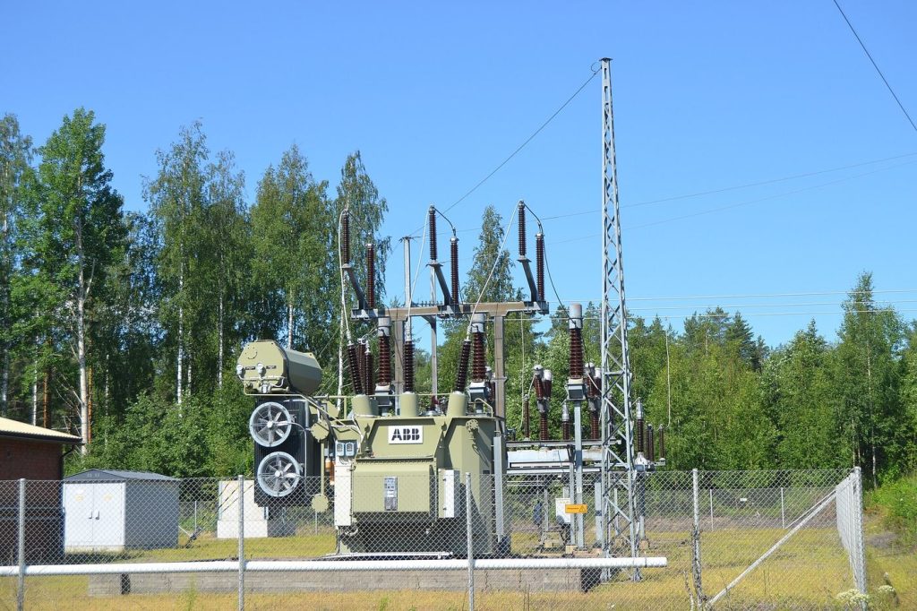 An electrical substation with transformers against a forest backdrop
